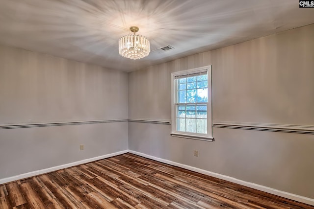 empty room featuring a chandelier, wood finished floors, and baseboards