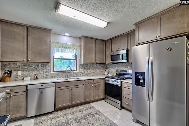 kitchen featuring appliances with stainless steel finishes, a sink, a textured ceiling, tasteful backsplash, and light countertops