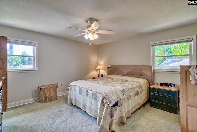 bedroom with multiple windows, light carpet, ceiling fan, baseboards, and a textured ceiling