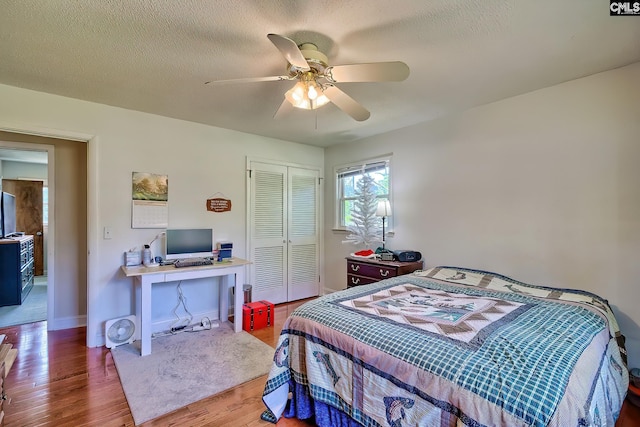 bedroom with an office area, a closet, wood finished floors, ceiling fan, and baseboards