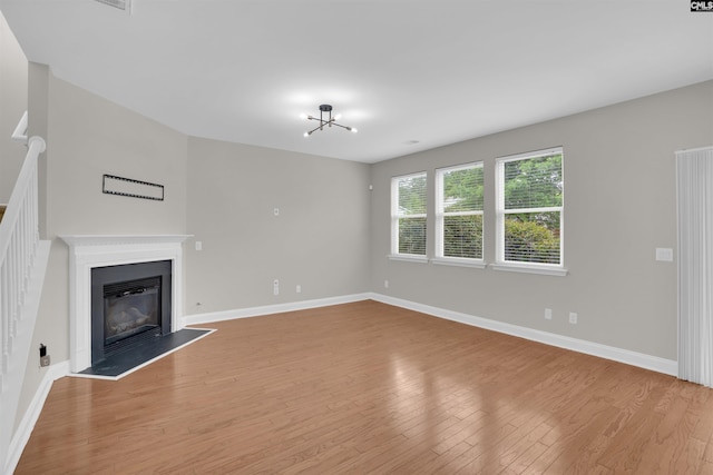 unfurnished living room with light wood-type flooring, baseboards, and a glass covered fireplace