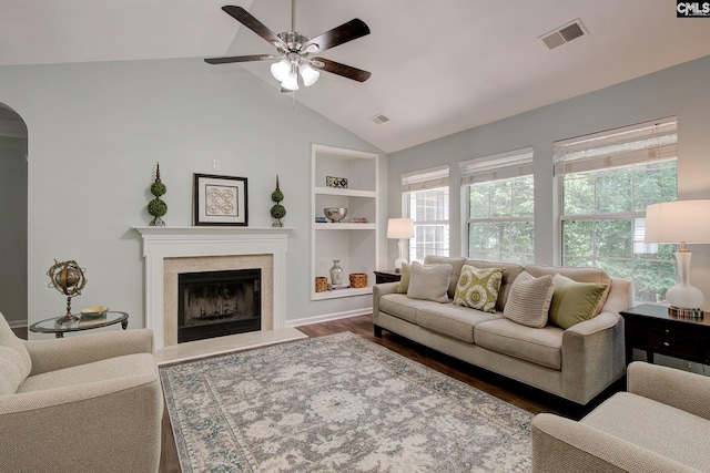 living area with a ceiling fan, built in features, arched walkways, a fireplace, and wood finished floors