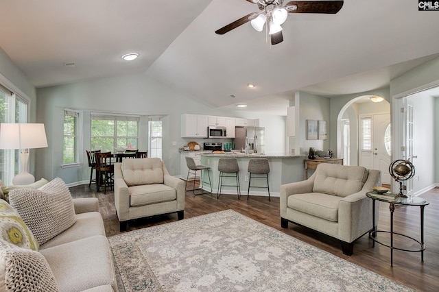 living area featuring healthy amount of natural light, ceiling fan, lofted ceiling, dark wood finished floors, and arched walkways