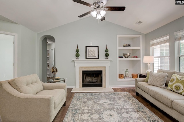 living area featuring vaulted ceiling, ceiling fan, dark wood-style flooring, built in shelves, and a premium fireplace