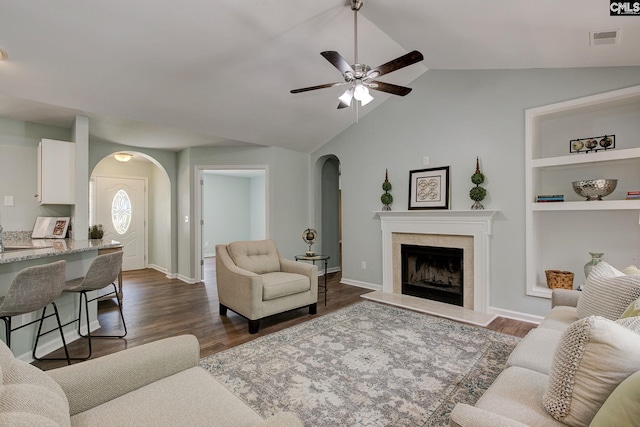 living room with arched walkways, ceiling fan, a premium fireplace, dark wood finished floors, and vaulted ceiling
