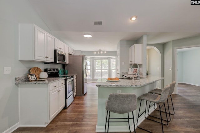 kitchen with appliances with stainless steel finishes, a sink, a breakfast bar, white cabinets, and dark wood finished floors