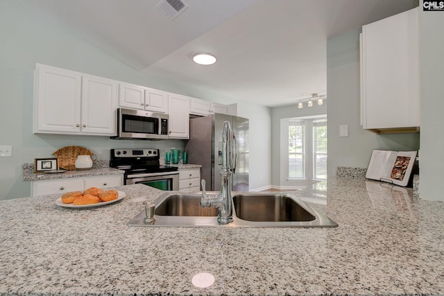 kitchen featuring stainless steel appliances, white cabinets, a sink, light stone countertops, and lofted ceiling