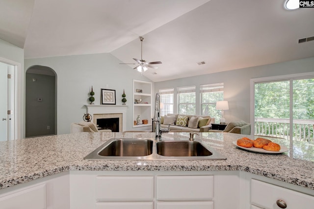 kitchen featuring a sink, vaulted ceiling, white cabinetry, a ceiling fan, and a fireplace