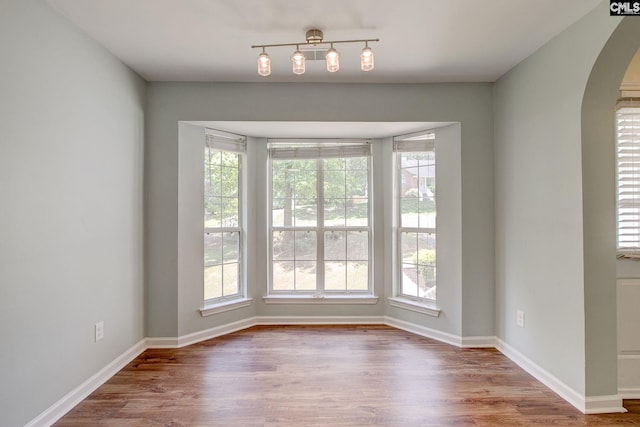 unfurnished dining area featuring arched walkways, wood finished floors, and baseboards