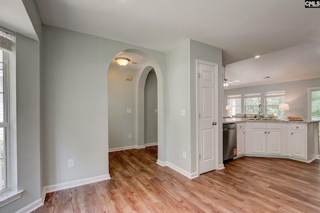 interior space with stainless steel dishwasher, arched walkways, white cabinetry, light wood-type flooring, and light stone countertops