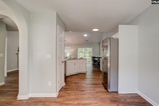 hall with arched walkways, light wood finished floors, baseboards, recessed lighting, and a sink