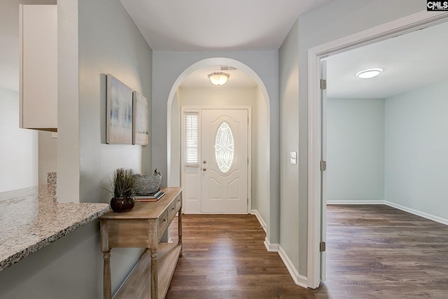 entrance foyer featuring dark wood-type flooring, arched walkways, and baseboards