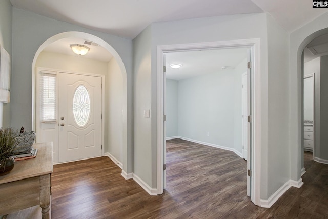 foyer entrance with arched walkways, dark wood-type flooring, and baseboards