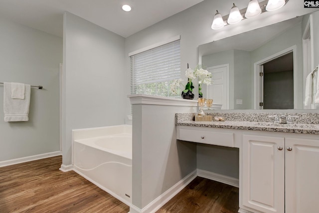bathroom featuring wood finished floors, a bath, vanity, baseboards, and recessed lighting