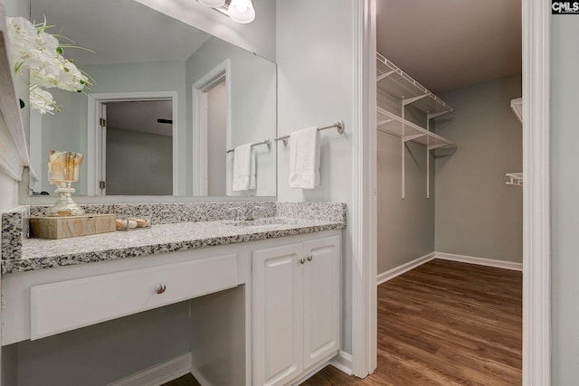 bathroom with wood finished floors, vanity, baseboards, and a walk in closet