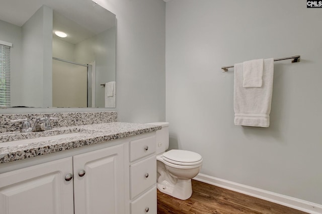 bathroom with wood finished floors, a stall shower, toilet, vanity, and baseboards