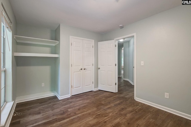 unfurnished bedroom featuring dark wood-style floors, baseboards, a closet, and multiple windows