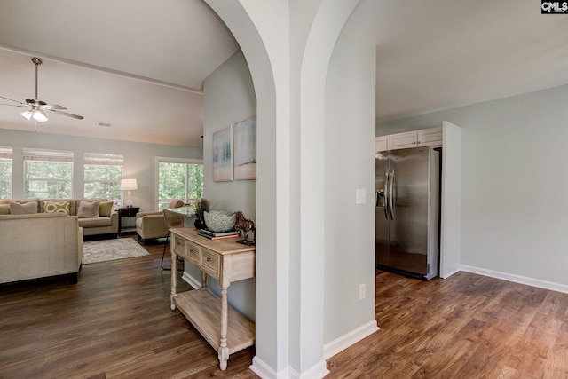 corridor featuring arched walkways, dark wood-style floors, baseboards, and lofted ceiling