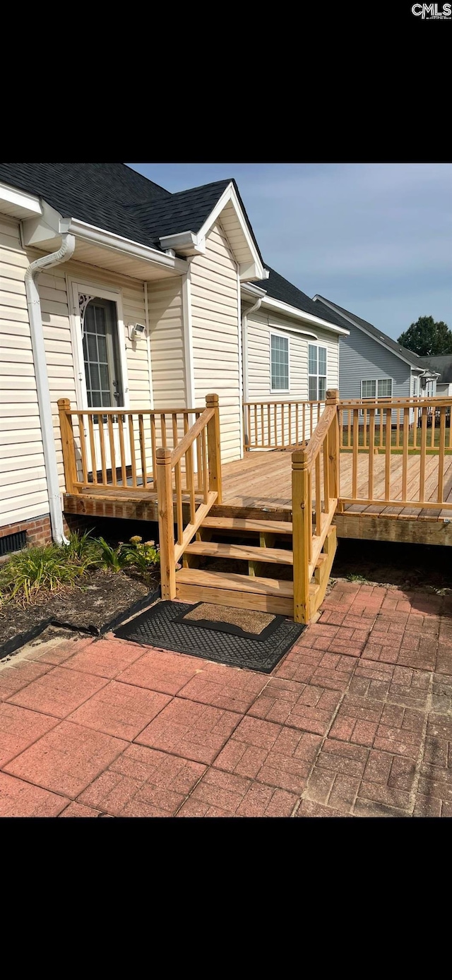 property entrance with a wooden deck and roof with shingles