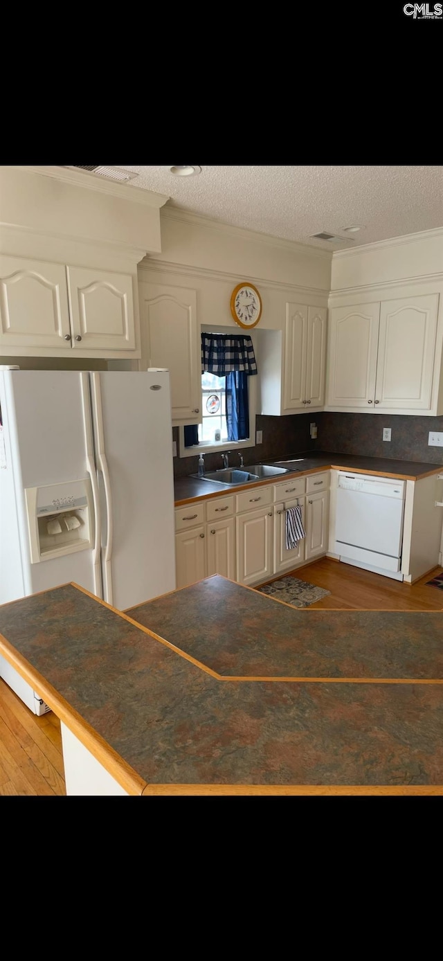 kitchen with white appliances, dark countertops, a sink, and white cabinets