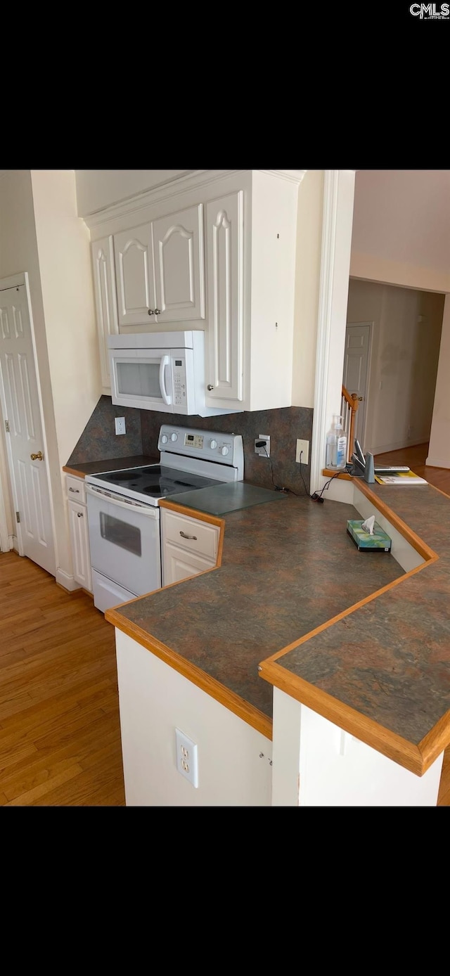 kitchen with white appliances, dark countertops, a peninsula, and white cabinetry