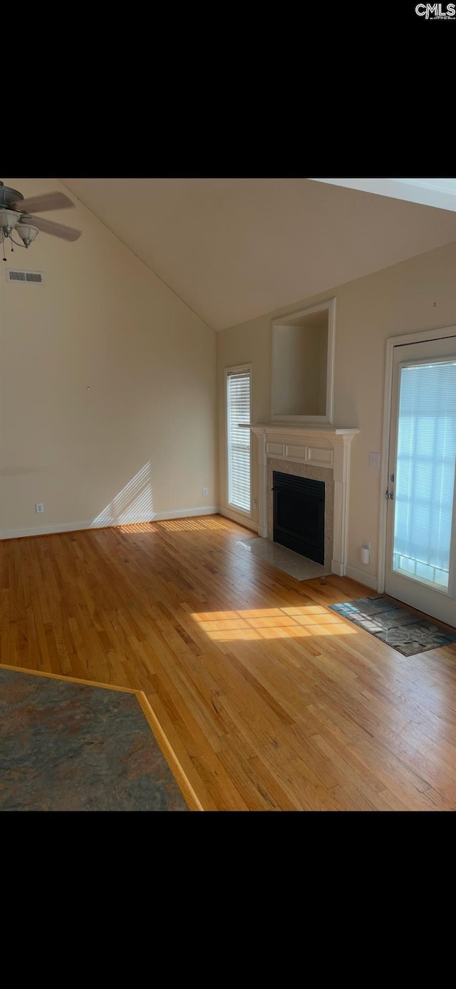 unfurnished living room featuring wood finished floors, lofted ceiling, a ceiling fan, a fireplace with flush hearth, and baseboards