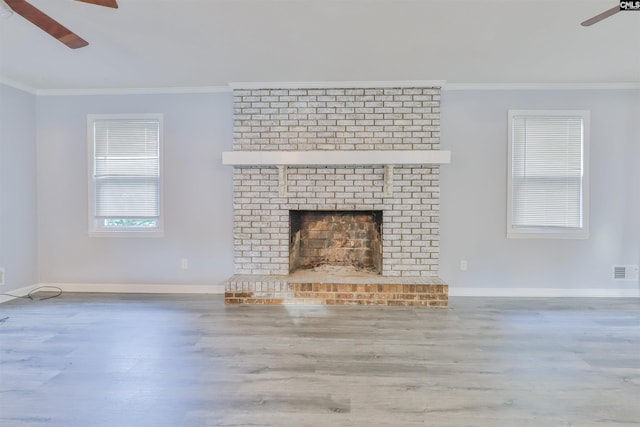 unfurnished living room featuring a ceiling fan, crown molding, wood finished floors, baseboards, and a brick fireplace