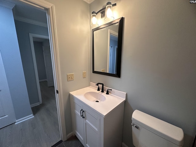bathroom with crown molding, wood finished floors, vanity, toilet, and baseboards