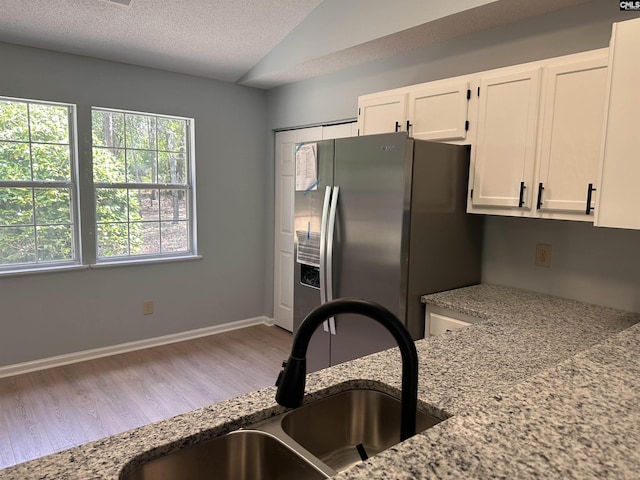kitchen featuring stainless steel refrigerator with ice dispenser, a sink, white cabinetry, wood finished floors, and light stone counters