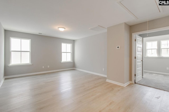 spare room with attic access, light wood-type flooring, and baseboards