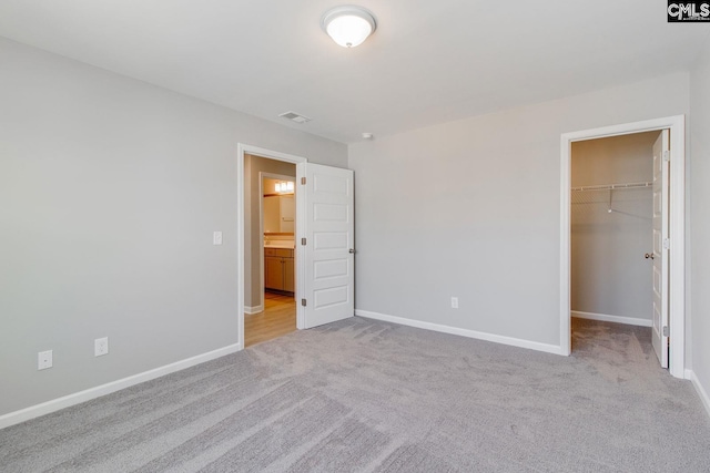 unfurnished bedroom with carpet floors, a walk in closet, baseboards, and a closet