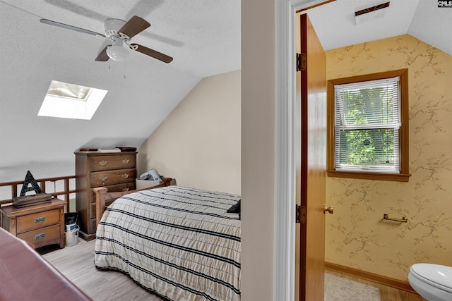 bedroom with wood finished floors, vaulted ceiling, a skylight, a textured ceiling, and ceiling fan