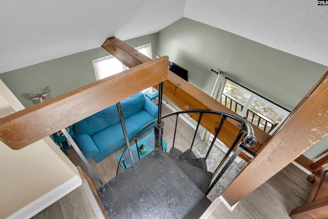 stairs with wood finished floors, vaulted ceiling, plenty of natural light, baseboards, and a textured ceiling