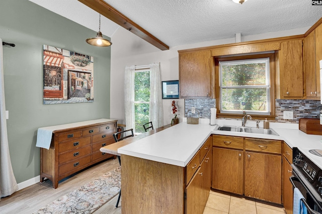 kitchen with a sink, a peninsula, tasteful backsplash, light countertops, and beam ceiling