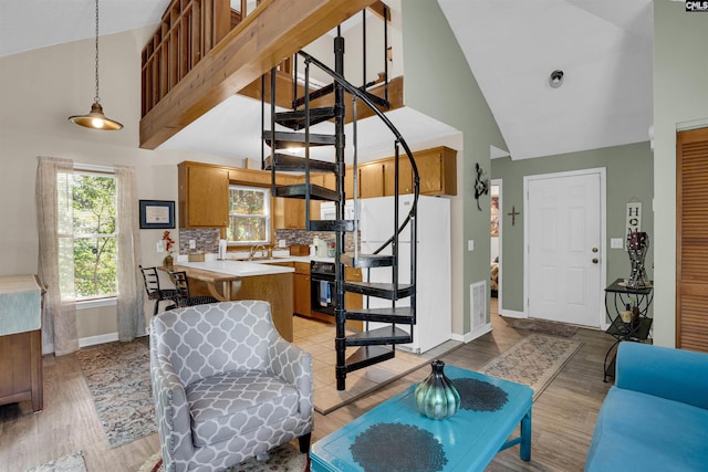 living room with high vaulted ceiling, light wood-style flooring, stairway, and baseboards