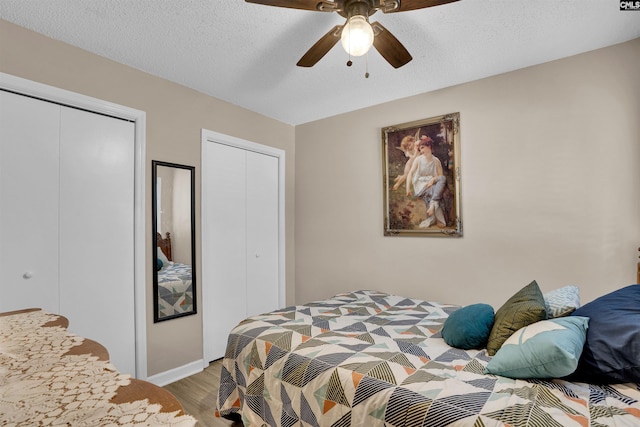 bedroom featuring multiple closets, wood finished floors, a ceiling fan, baseboards, and a textured ceiling