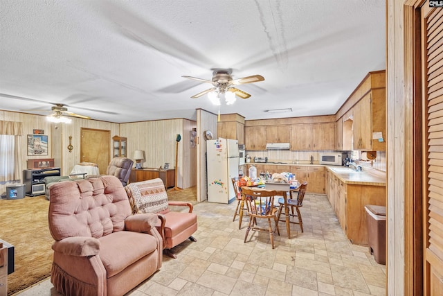 living area featuring ceiling fan, a textured ceiling, wood walls, and light stone finish floors