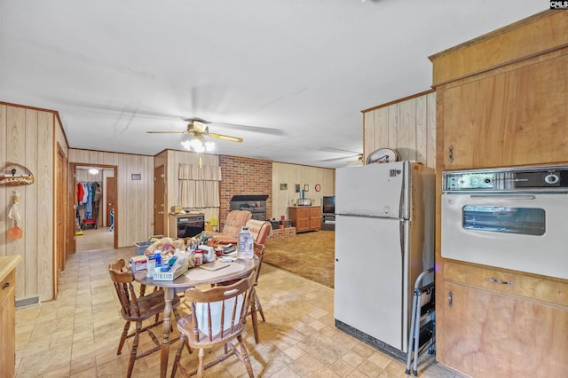 dining space featuring wood walls, ceiling fan, and a brick fireplace