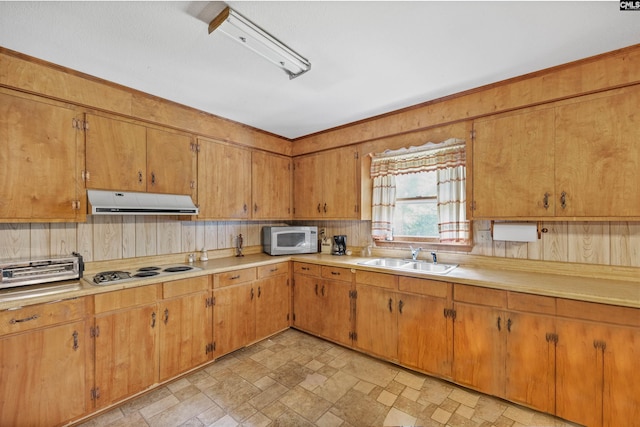 kitchen with white microwave, a sink, cooktop, under cabinet range hood, and light countertops