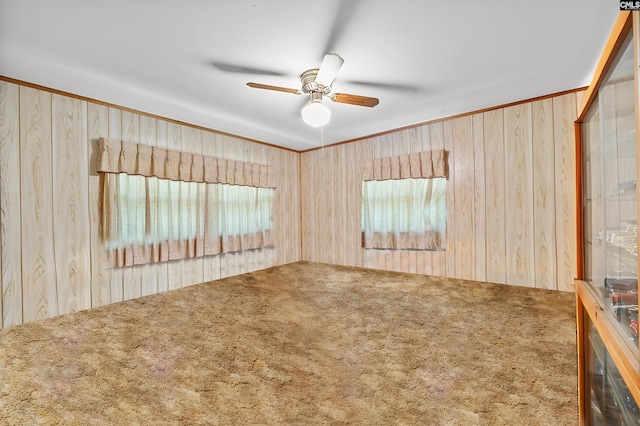 spare room with carpet, wooden walls, a ceiling fan, and ornamental molding