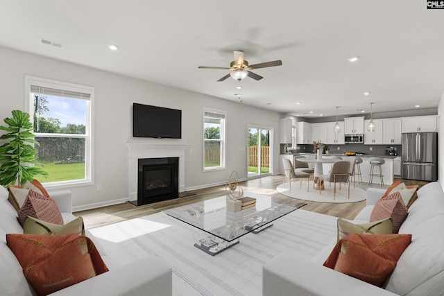 living area featuring a glass covered fireplace, light wood-style floors, recessed lighting, a ceiling fan, and baseboards