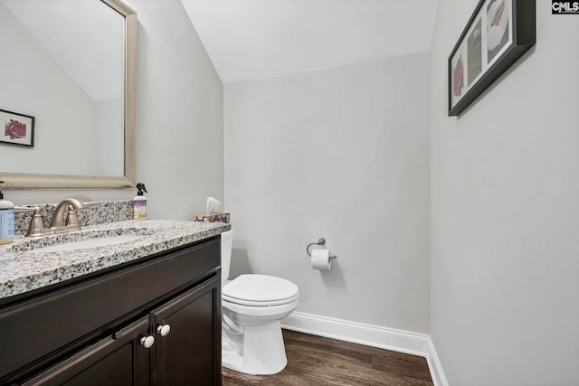 half bath with lofted ceiling, wood finished floors, toilet, vanity, and baseboards