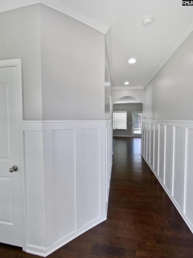 hallway with arched walkways, crown molding, wood finished floors, a decorative wall, and a wainscoted wall