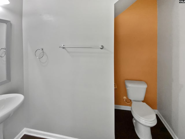 half bath featuring toilet, baseboards, and a sink