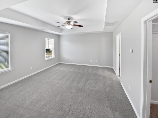 spare room featuring a tray ceiling, ceiling fan, carpet floors, and baseboards