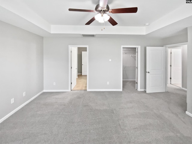 unfurnished bedroom featuring a raised ceiling, a walk in closet, carpet flooring, and baseboards