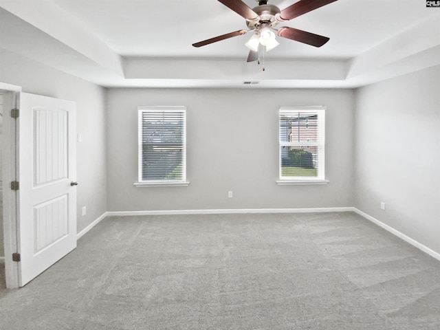 unfurnished room with carpet flooring, ceiling fan, a raised ceiling, and baseboards