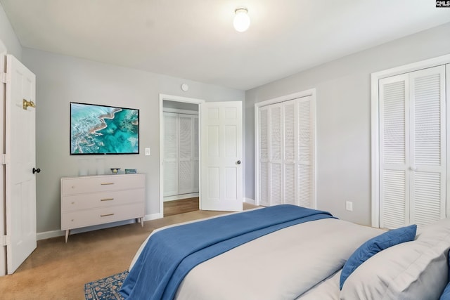 bedroom featuring multiple closets, light colored carpet, and baseboards