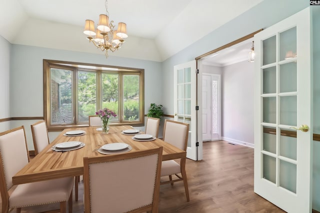 dining room with a chandelier, wood finished floors, lofted ceiling, and baseboards