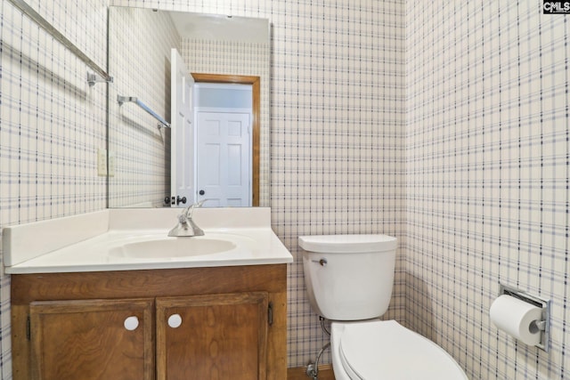 half bathroom featuring wallpapered walls, toilet, and vanity